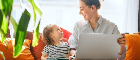 Child and mother looking at each other seated on a couch, mother holding a laptop