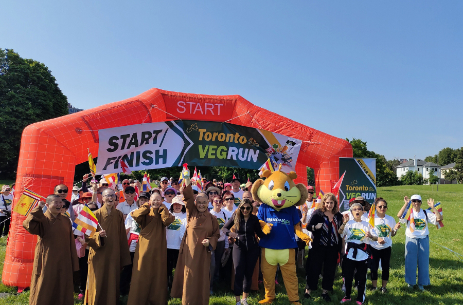 A group of people, including squirrel mascot "Erin" smiling and posing with VEGRUN signage being held up by an inflatable banner.