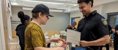 Joseph receives a certificate presented by a police officer at ErinoakKids in the Reach For It! program  