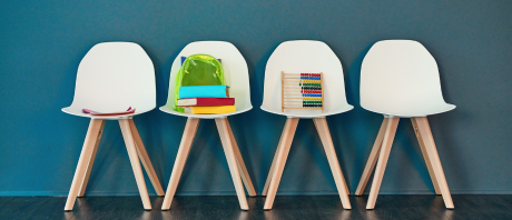 Four white chairs side by side with books and toys on them