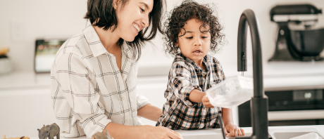 A toddler washes a container with parent support