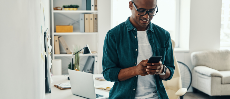 A man using his phone with laptop in the background