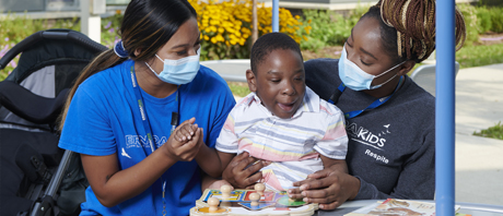 Two women wearing masks attend to a young boy