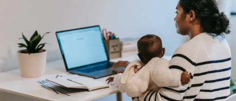 A mother with her young child on a laptop at her desk
