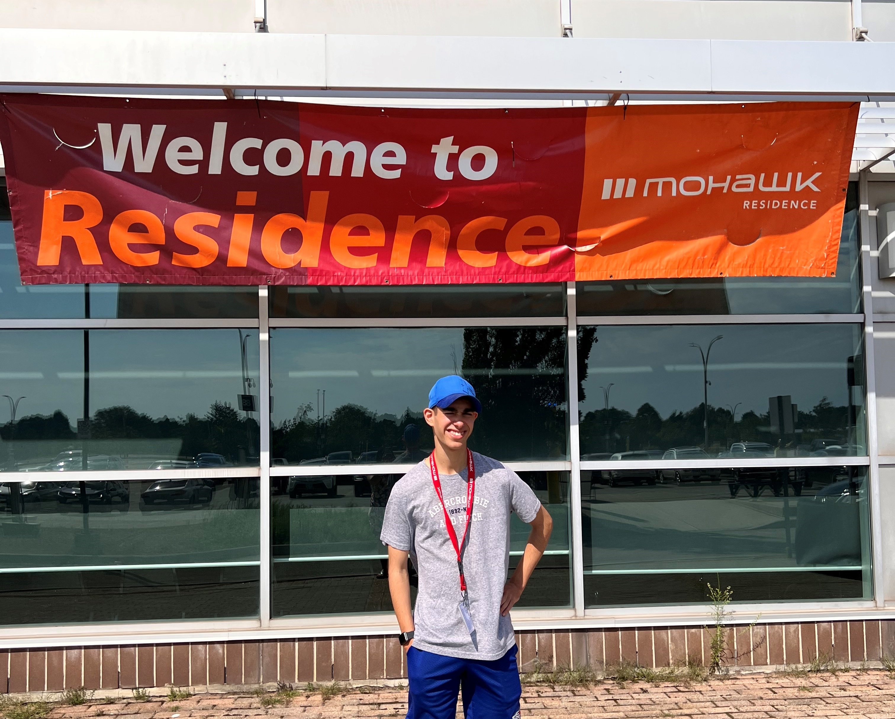 Jayden stands in front a of banner that reads "welcome to residence"