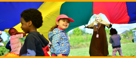 A clinician holds a rainbow tent up and multiple young clients are running under it