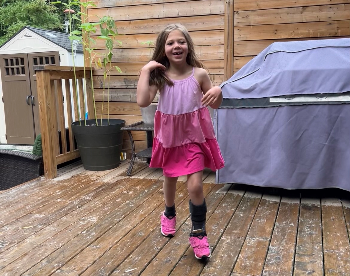 Mikayla smiling wearing a pink dress with a leg brace on her left leg
